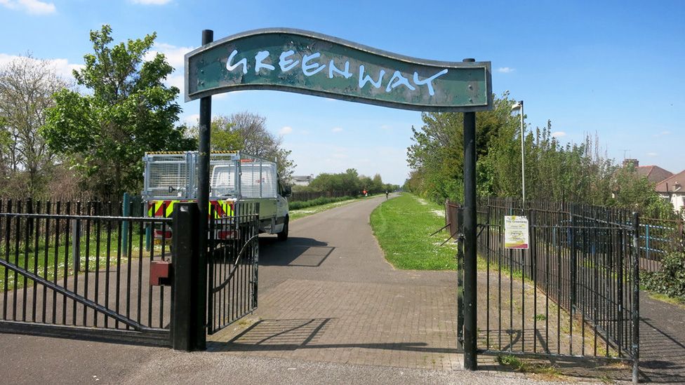 The Greenway green sign to the route with fence and public vehicle in background