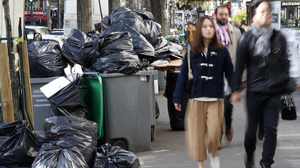 People walk past bins that overflow with bags of garbage during a strike by rubbish collectors in Paris.