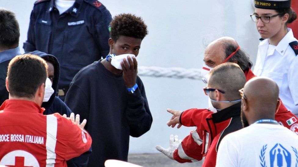 A migrant holds breathing mask to his face