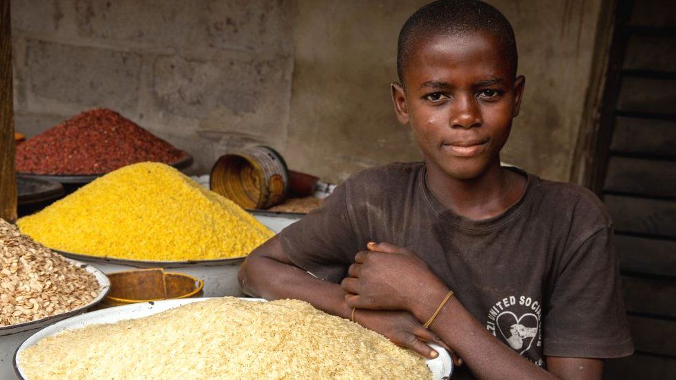 Мальчик позирует рядом с рисом в своем магазине на рынке Аджарии