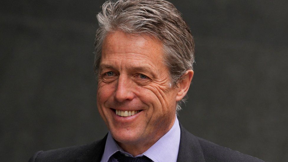 Hugh Grant smiles outside the High Court, in London