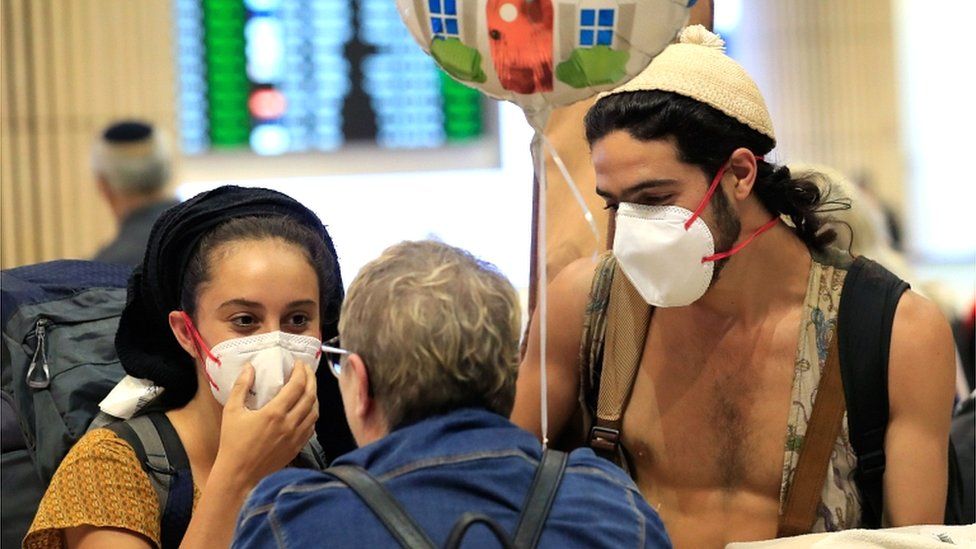 A young couple wearing protective masks are greeted upon arrival at Ben Gurion airport in Tel Aviv on 4 March 2020