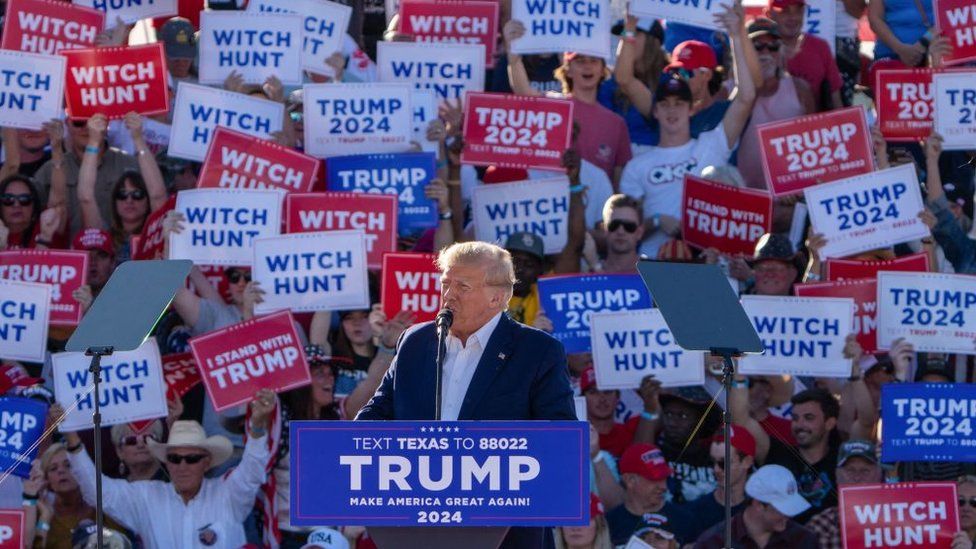 Supporters hold 'Witch Hunt' signs as Donald Trump speaks at a March 2023 campaign rally