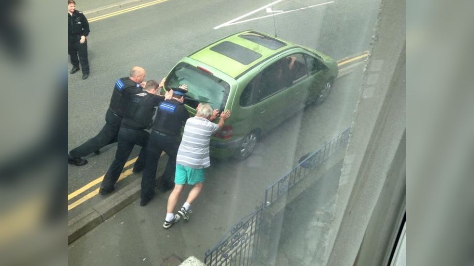Three police officers and a resident pushing a car off the pavement