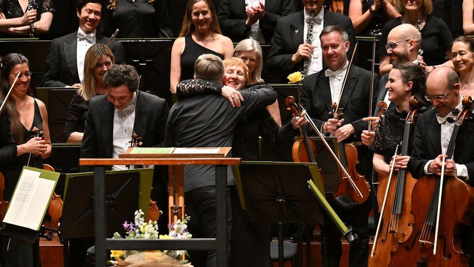 Jacoba Gale and Kirill Karabits embracing at her final concert in Poole while the rest of the orchestra look on