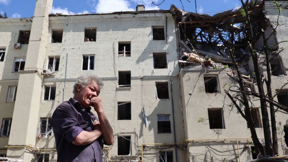 man stands in front of the completely damaged building in Ukrainian city of Mariupol