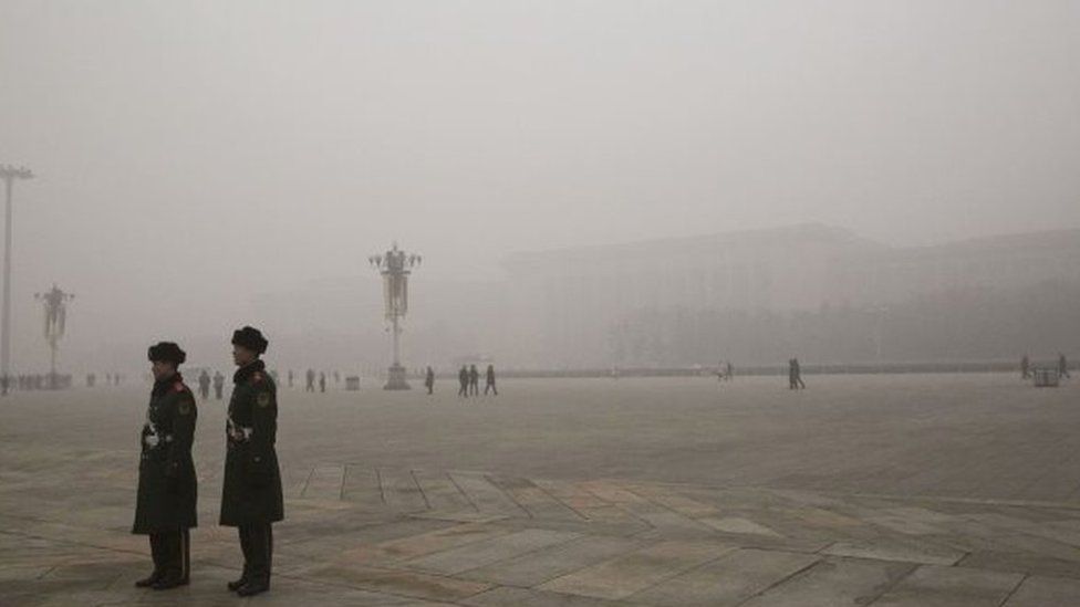 In this composite of two separate images, Chinese Paramilitary officers stand Tiananmen Square and the Great Hall of the People is seen in heavy pollution, top, on December 1 and 24 hours later under a clear sky on December 2, 2015 in Beijing, China