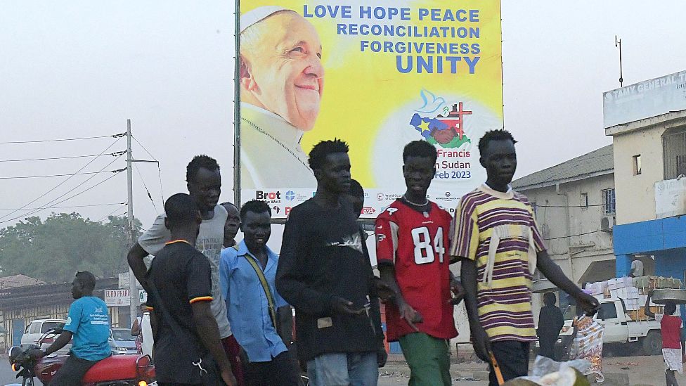 A group of young people walk past a banner showing the portrait of Pope Francis as preparations continue ahead of his visit in Juba, South Sudan - 31 January 2023