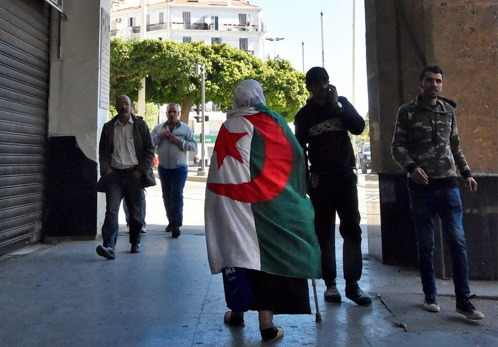 An elderly Algerian woman wrapped in a national flag walks through a colonnade in Algiers.