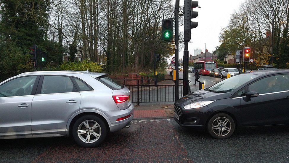 Cars stopped across pedestrian crossing as green man indicates pedestrians can cross