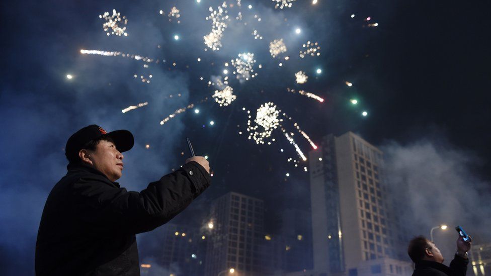 Two men photograph fireworks on a street in Beijing early on February 8, 2016