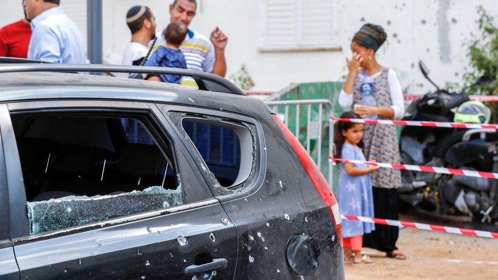 Israelis stand near a car damaged by a rocket fired from Gaza (9 August 2018)
