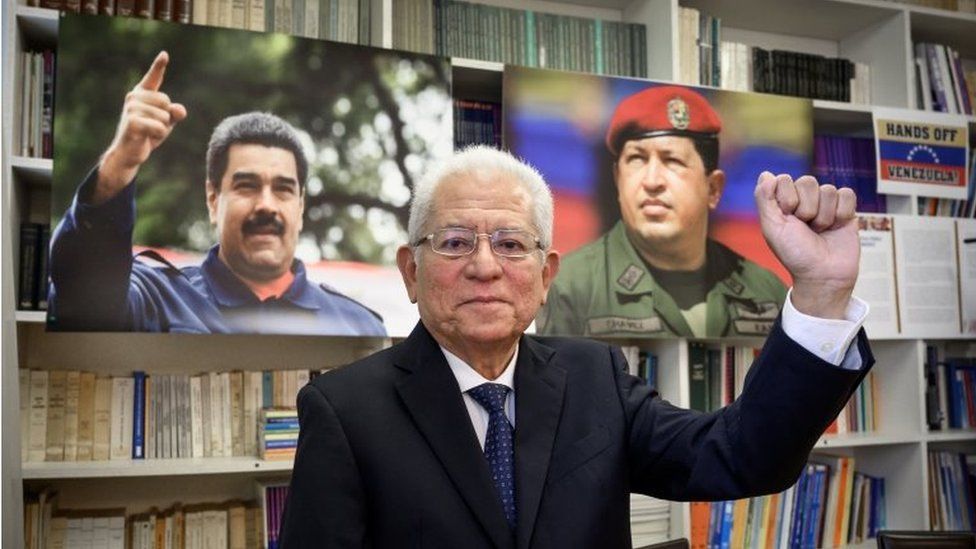 Ambassador Jorge Valero poses between photographs of President Nicolas Maduro (L) and late President Hugo Chavez during a interview with AF