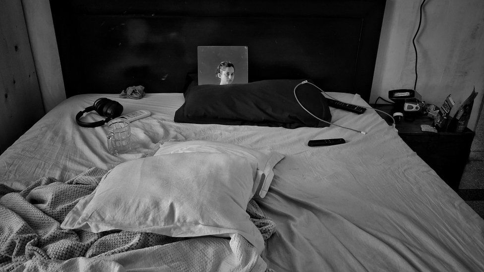 Photograph of Aparna's bed, with her face reflecting back in a mirror