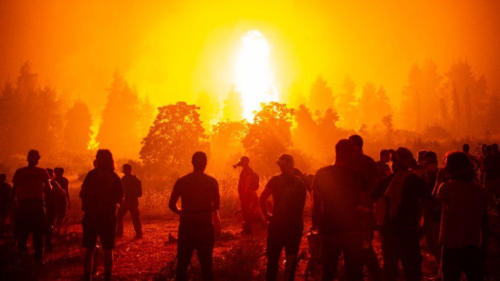 A silhouette of firefighters looking towards a large fire