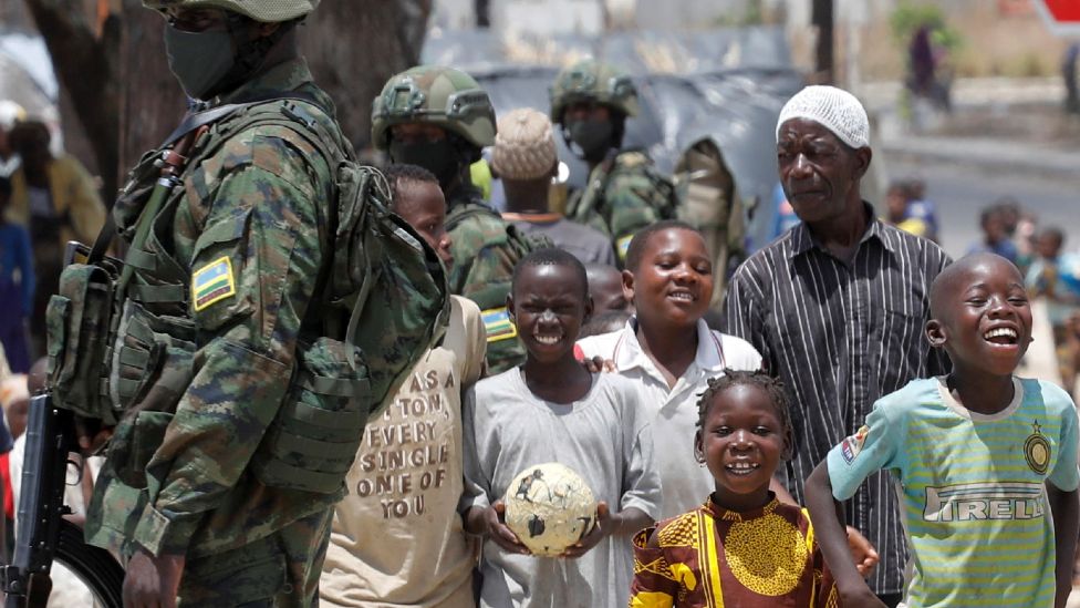 Children displaced by fighting walk past soldiers from the Rwandan security forces in a camp for the internally displaced, in the town of Quitunda, Mozambique - 22 September 2021