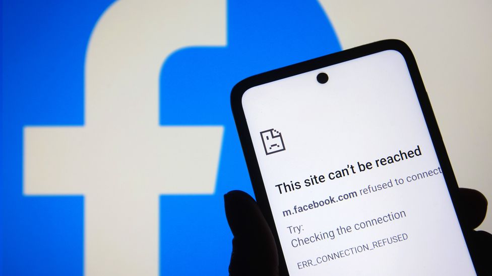Stock image of a message that says, "This site can't be reached," is seen on a smartphone screen with a Facebook logo in the background