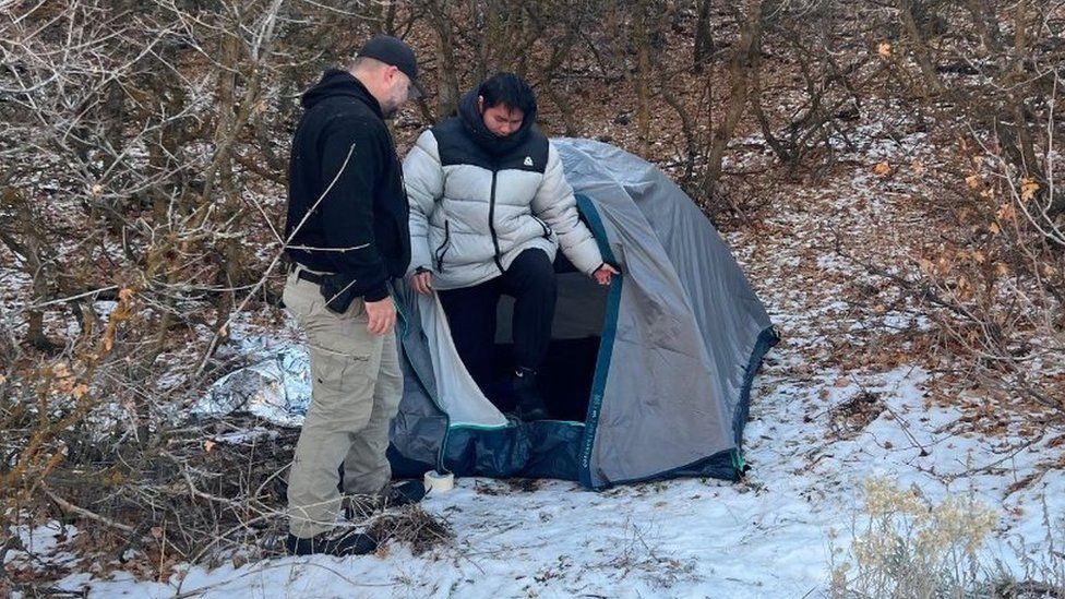 Kai Zhuang climbs out of a tent as an officer looks on