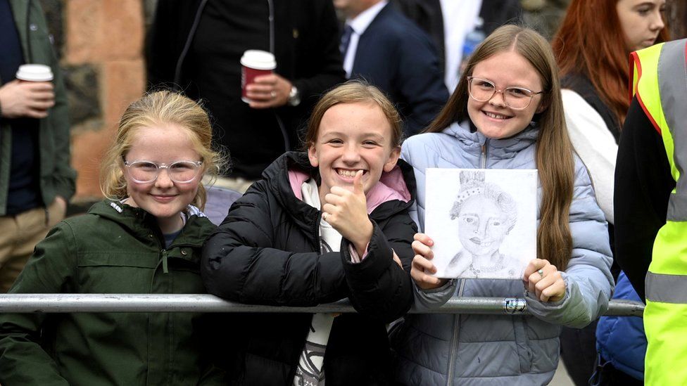 Three young girls - including one holding a portrait of Queen Elizabeth II - smile after meeting the King and Camilla outside Hillsborough Castle