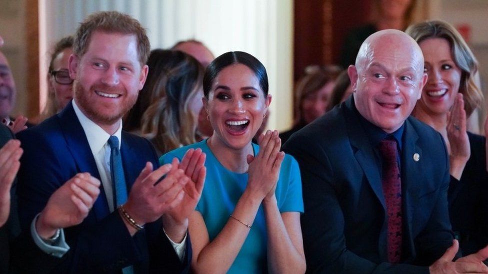 Prince Harry, Meghan and Ross Kemp, cheering.