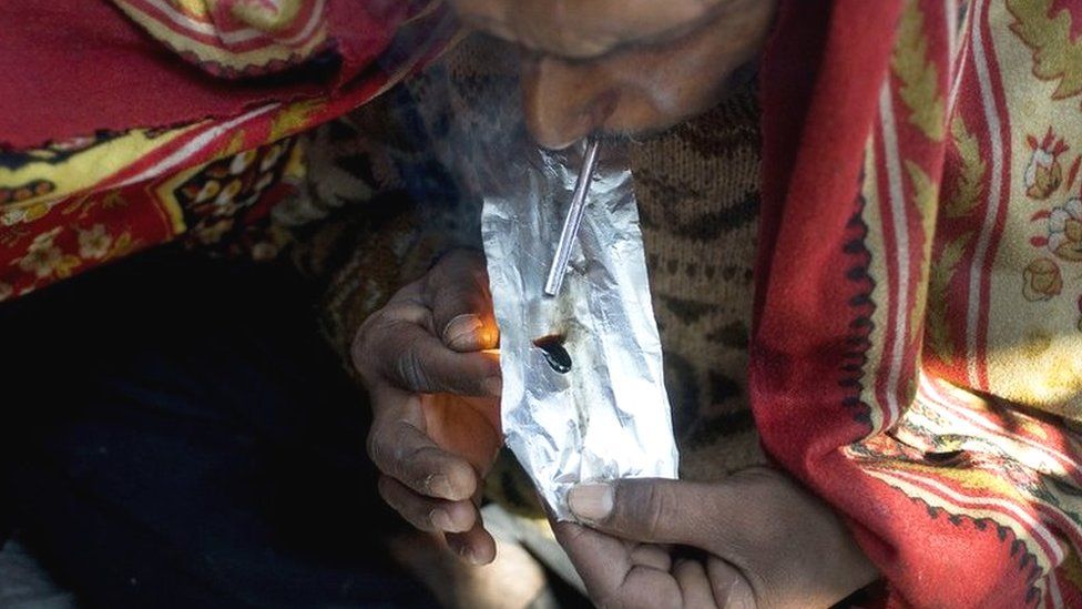 Idian drug user covers himself with a blanket as he smokes smack, heroin, in old Delhi