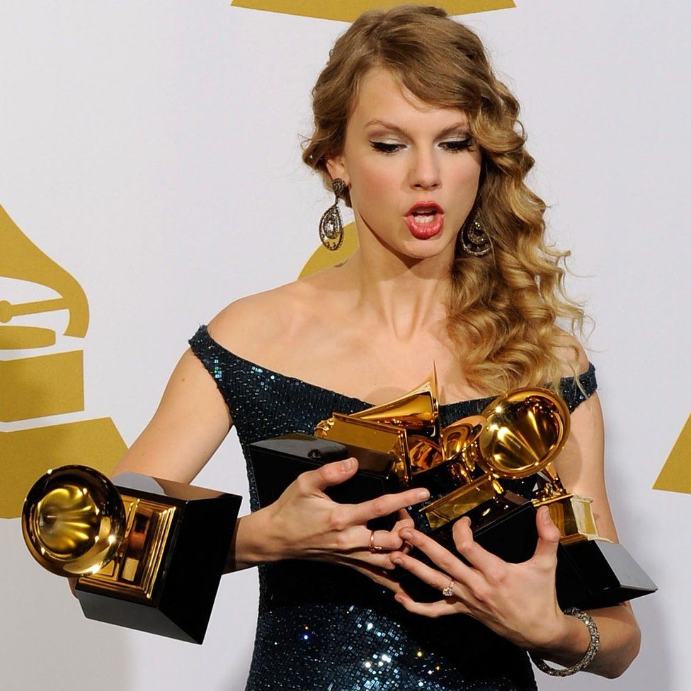 Taylor Swift holding an armful of Grammy Awards, but losing grip of one which drops to the floor