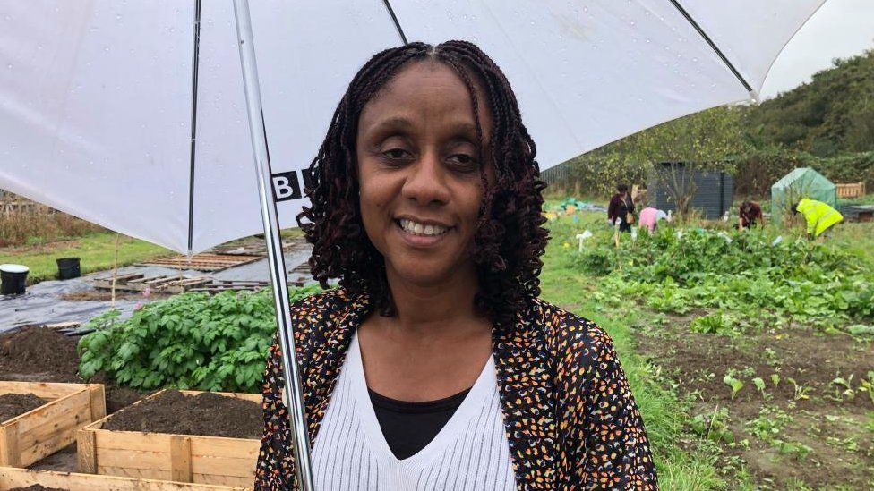 Woman with long dark hair holds an umbrella in an allotment