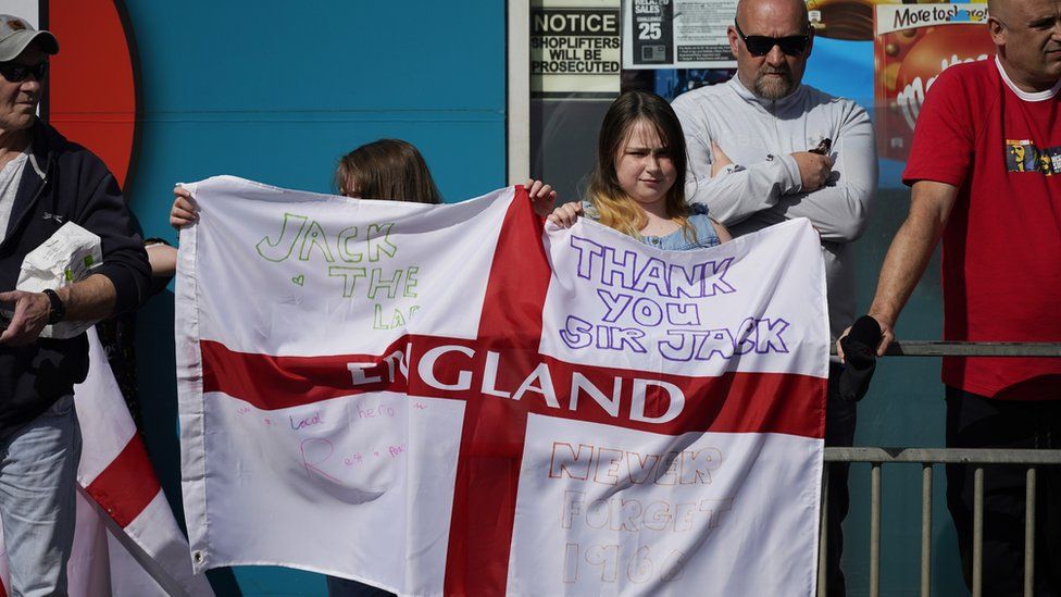 Two youngsters hold up an England flag with messages celebrating Jack Charlton