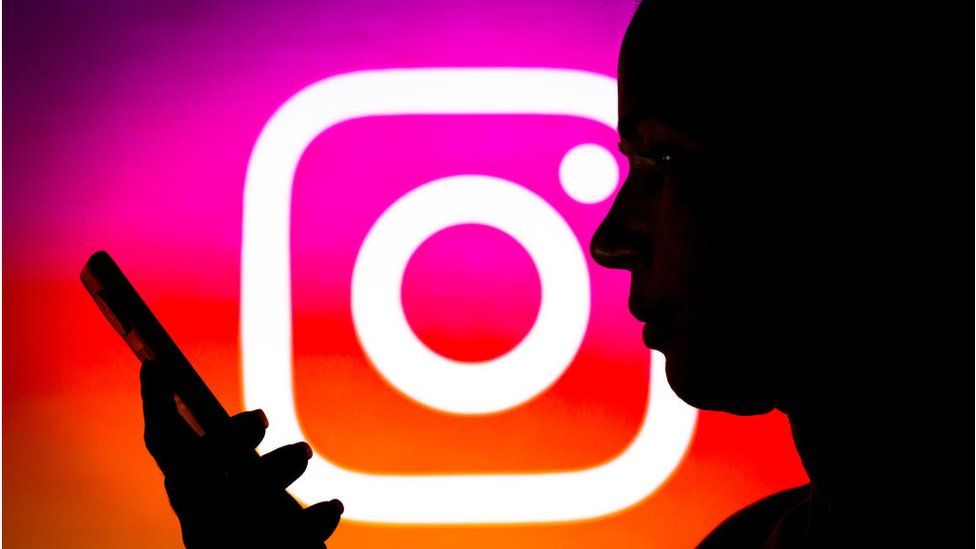 Женщина с телефоном и логотипом Instagram на заднем плане