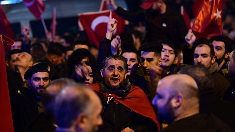 People gesture and wave flags as Turkish residents of the Netherlands gather for a protest outside Turkey's consulate in Rotterdam on March 11, 2017