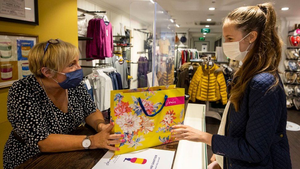 Mary Rogan, shop assistant at Joules in Belfast, hands Ella Copper her purchase while wearing a face mask as face coverings are now compulsory for shoppers in Northern Ireland