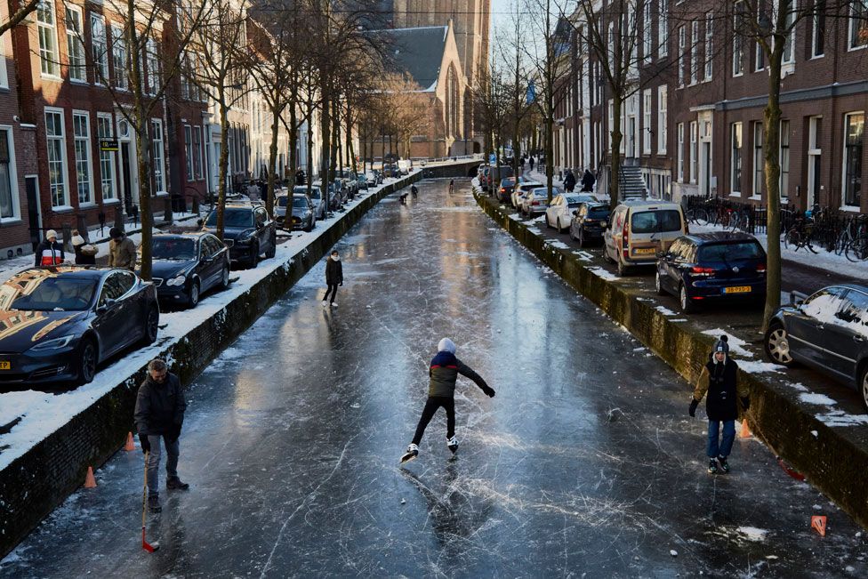 People skate on a frozen canal in a residential area of the Netherlands