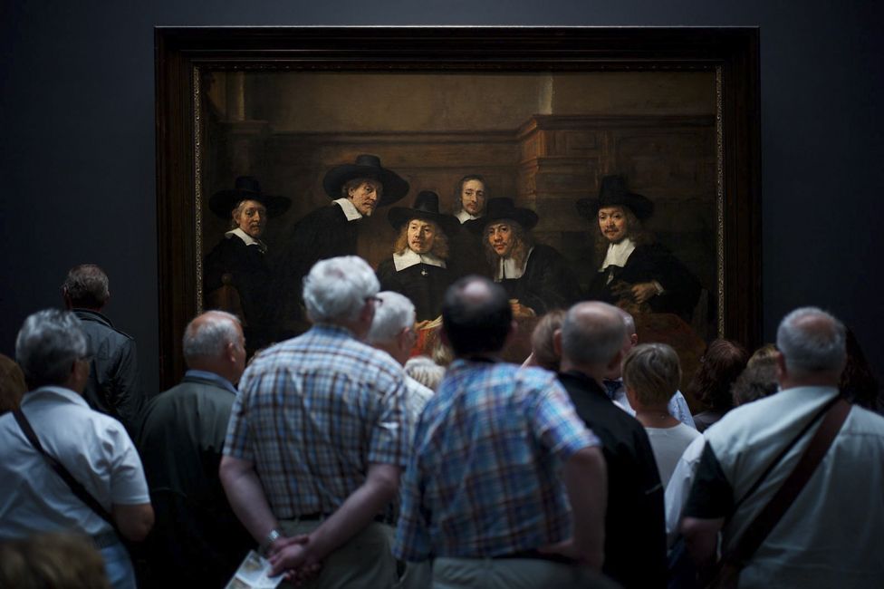 Museum visitors watching Rembrandt's painting Syndics of the Drapers' Guild