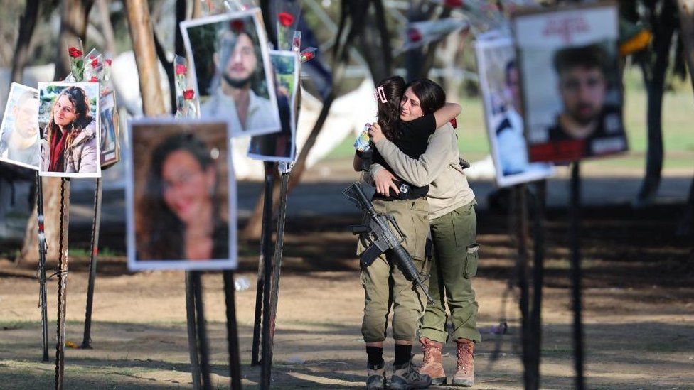 Israeli soldiers hug as they look at pictures of the Nova music festival victims at the site of the festival near Kibbutz Reim