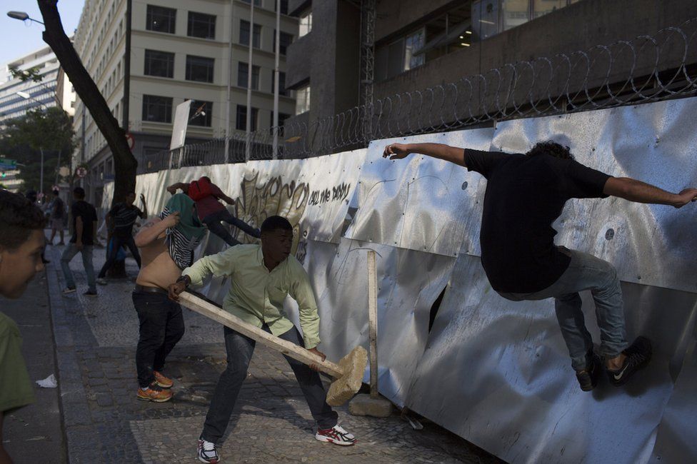 Anti-austerity demonstrators kick down the fence of a building, closed for construction, to build a road block near the state legislature where lawmakers are discussing austerity measures in Rio de Janeiro, Brazil, Tuesday, 6 December