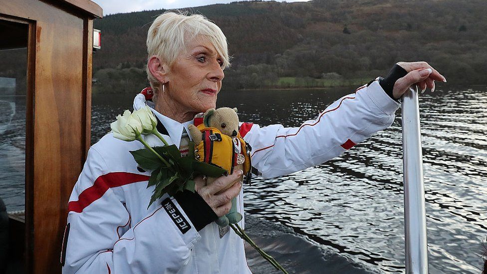Gina Campbell holding flowers and her father's mascot, Mr Whoppit, onboard a boat on Coniston Water on the 50th anniversary of his death