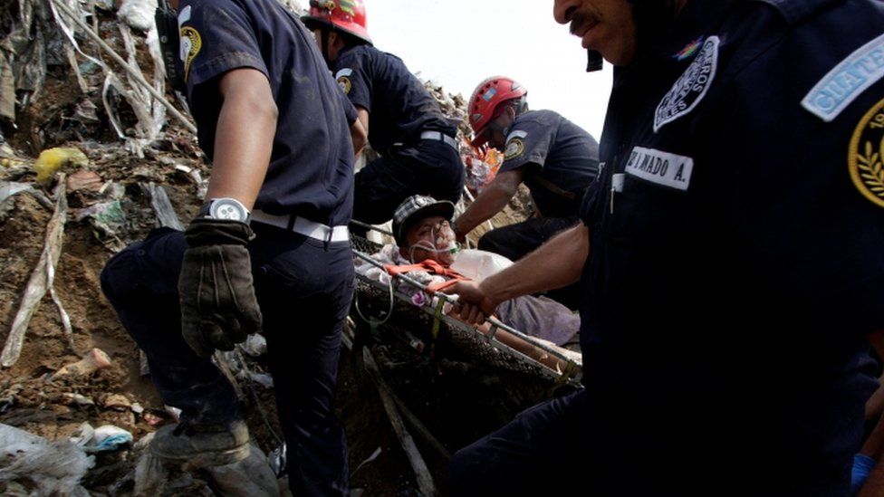 Firefighters carry a stretcher bearing a garbage collector, who was injured after a massive pile of garbage collapsed at a landfill dumpsite in Guatemala City