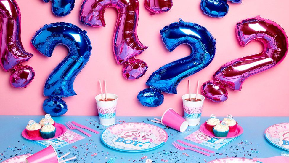 Gender reveal party merchandise, including inflatable blue and pink question marks, party plates and confetti