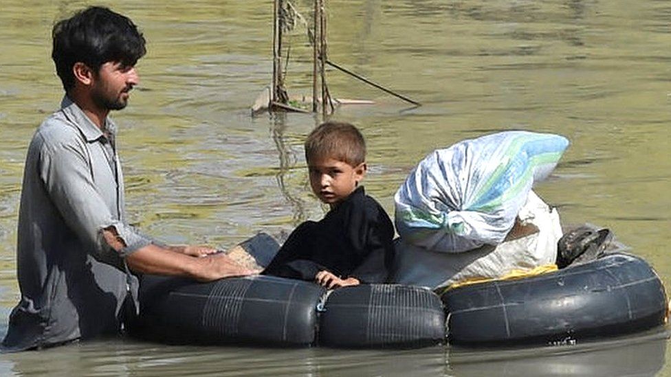 A man with child wades through a flood hit area following heavy monsoon rains in Charsadda district of Khyber Pakhtunkhwa.