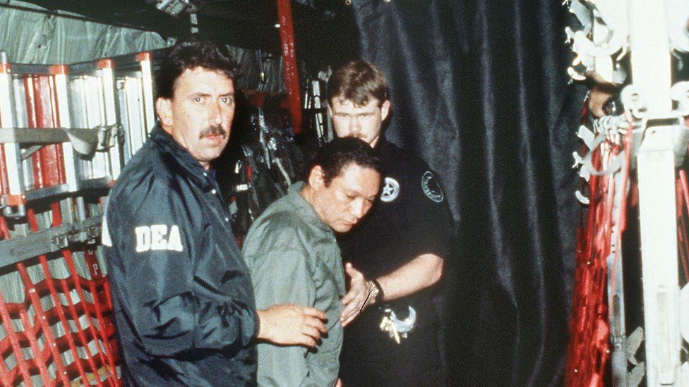 Panamanian General Manuel Noriega (C) is brought on board a US military plane 3 January 1990 for a flight to Miami after his arrest.