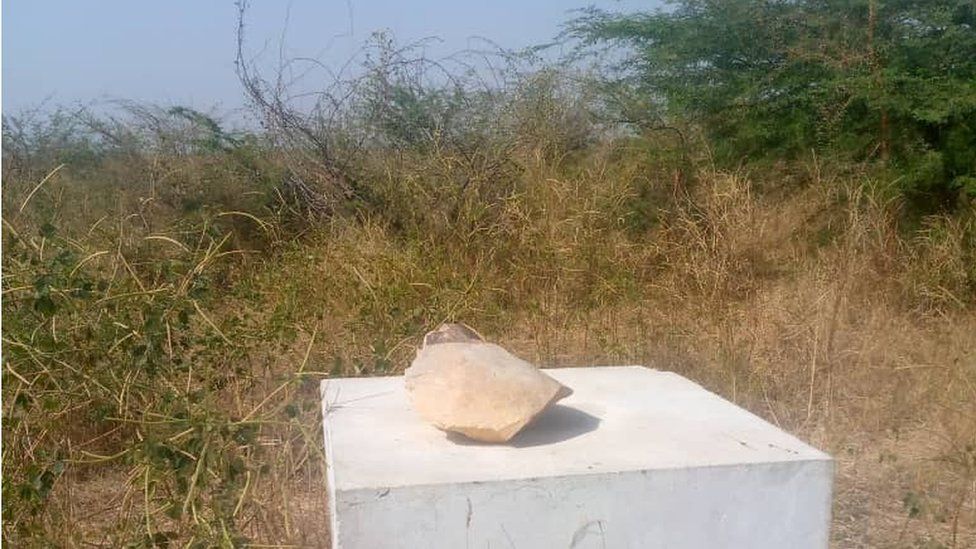A concrete block with a stone on top with scrub land behind it