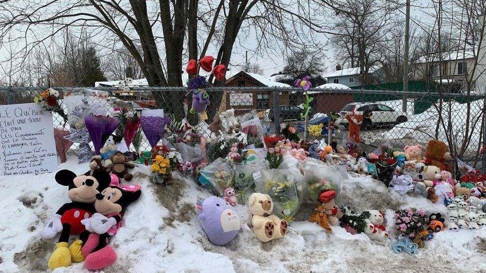 Photo of makeshift memorial outside of daycare in Laval, filled with flower bouquets and stuffed animals