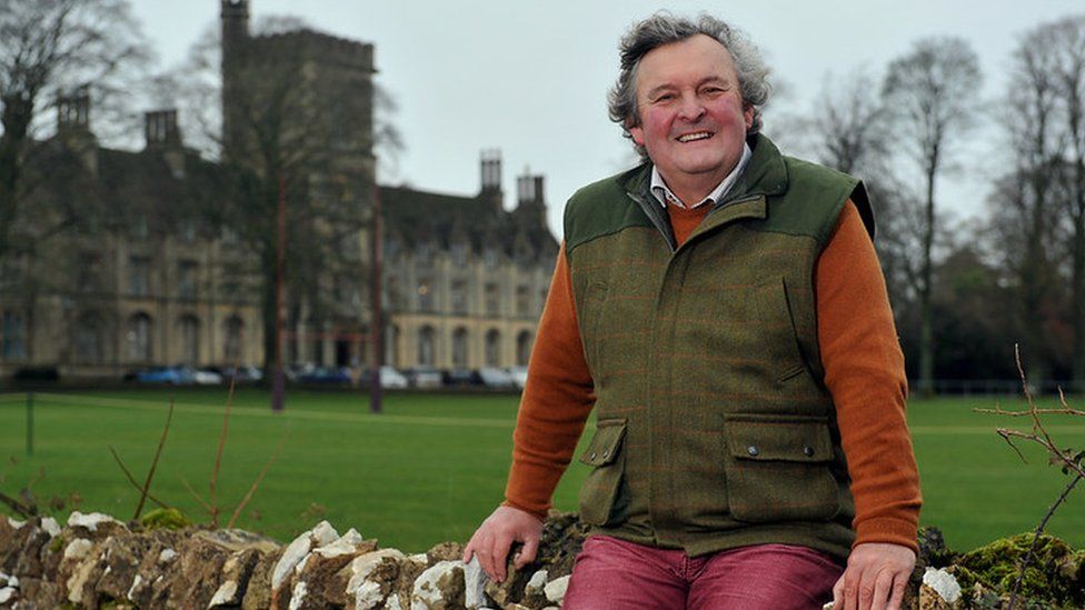 Prof Mark Horton sat on a traditional Cotswold stone wall outside the Royal Agricultural University