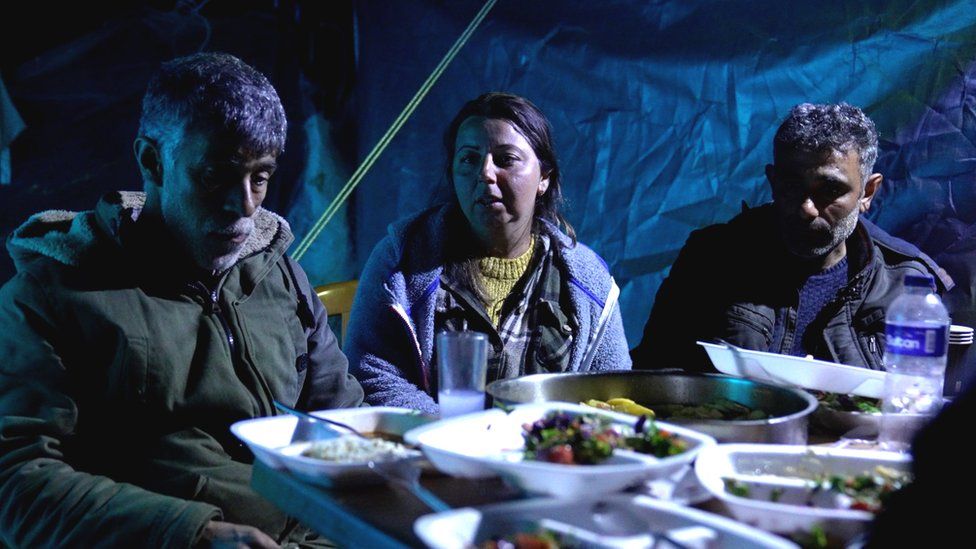 Songül Yücesoy (ortada) artık evsiz ve bir çadırın yanında yemek yiyor