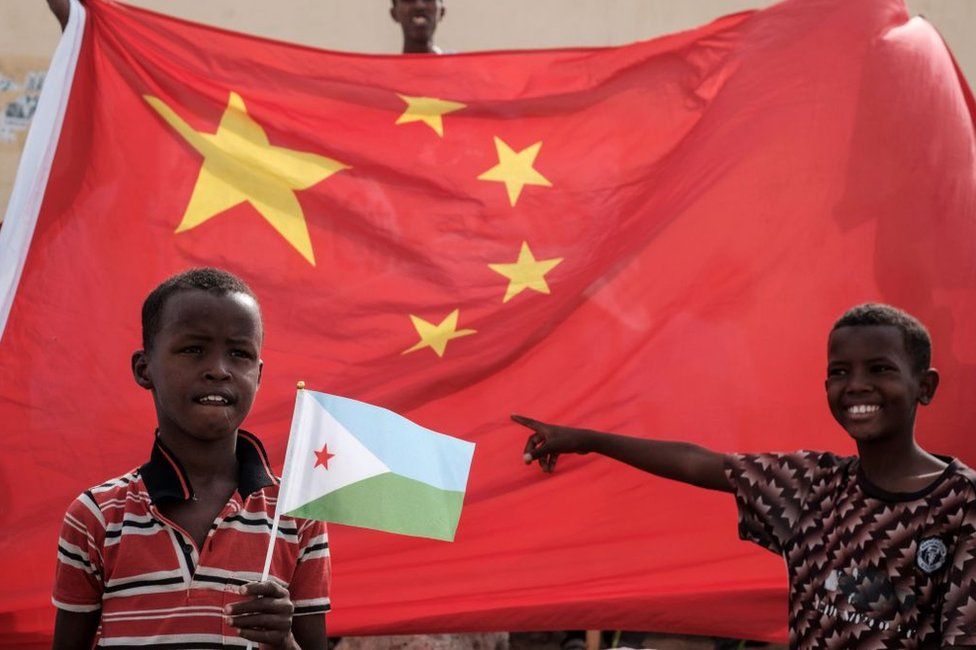 A boy holds Djiboutian national flag in front of Chinese national flag as he waits for Djibouti's President Ismail Omar Guellehas before the launching ceremony of new 1000-unit housing construction project in Djibouti, on July 4, 2018. - The new 1000-unit construction project by the Ismail Omar Guelleh Foundation for Housing is financially supported by China Merchant, the operation parther of newly inaugurated Djibouti International Free Trade Zone (DITTZ) with Djibouti Ports and Free Zones Authority, to build basic two bedroom apartments for low income people.