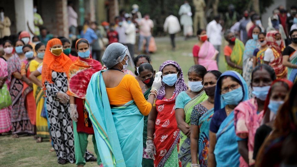 A health worker checks the temperature of women queuing outside a polling station during the sixth phase of the 2021 West Bengal Legislative Assembly election at Kampa village.