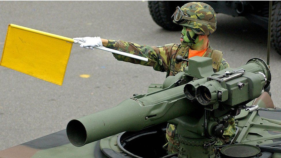 A Taiwanese soldier wearing camouflage uniform waves a flag from atop a armoured vehicle equiped with US-made TOW anti-tank missiles as it drives through Taipei's presidential office square during a rehearsal of the scheduled National Day military parade 08 October 2007