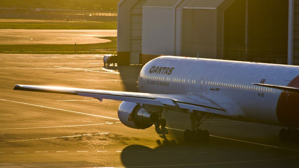 A Qantas plane pictured at sunset or sunrise outside an aircraft hanger.