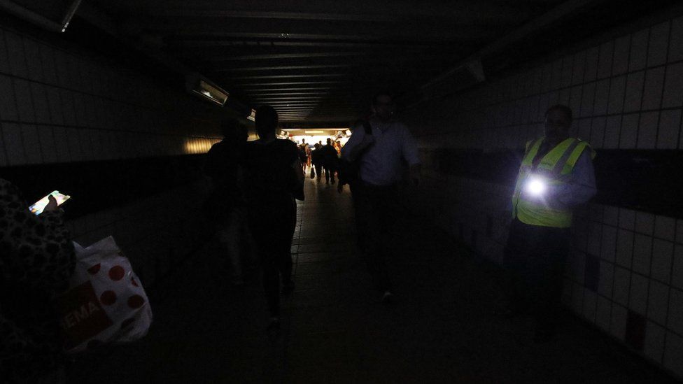 People walking in complete darkness at Clapham Junction station in London during a power cut,