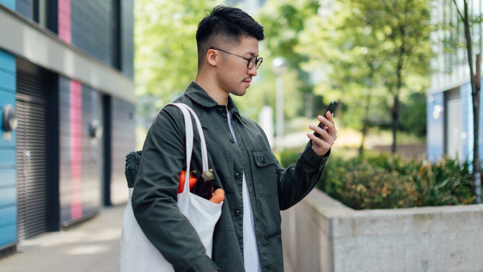 Man holding bag of groceries checks phone